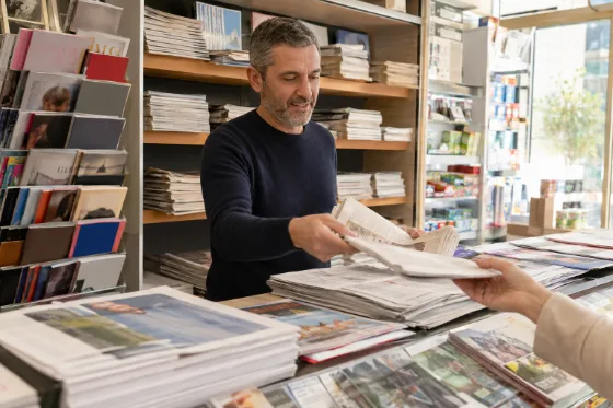 Un giornalaio che porge il quotidiano a una cliente