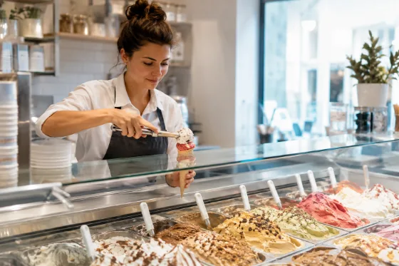 Una gelatiera che prepara un cono davanti alla vetrina